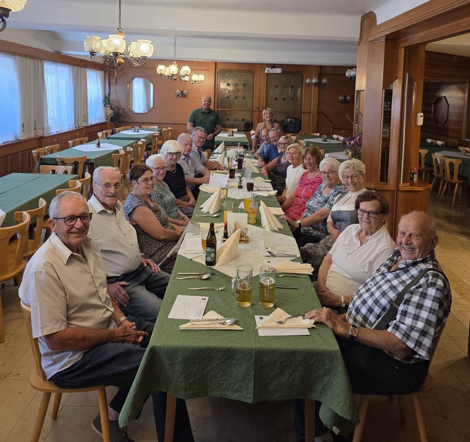 Gruppe von Menschen feiert gemeinsam bei einem Essen an einem langen Tisch in einem Restaurant.