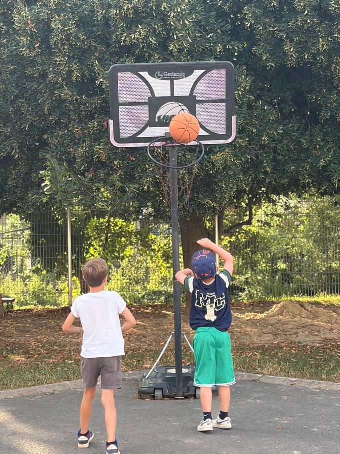 Zwei Kinder spielen Basketball auf einem Freiplatz im Grünen
