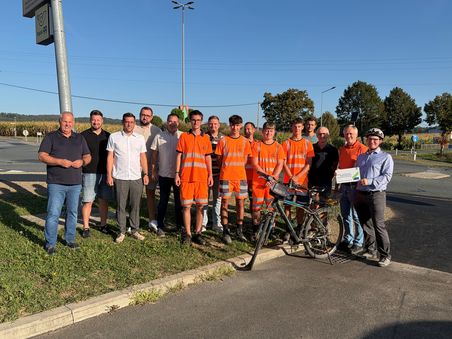 Gruppe von Männern in Arbeitskleidung und Zivilkleidung mit einem Fahrrad und einem Scheck in Niederösterreich